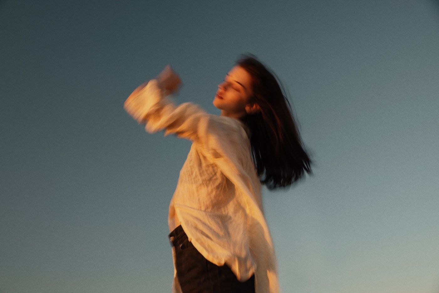 A woman in a cream shirt moving freely in warm evening light, hair in motion.