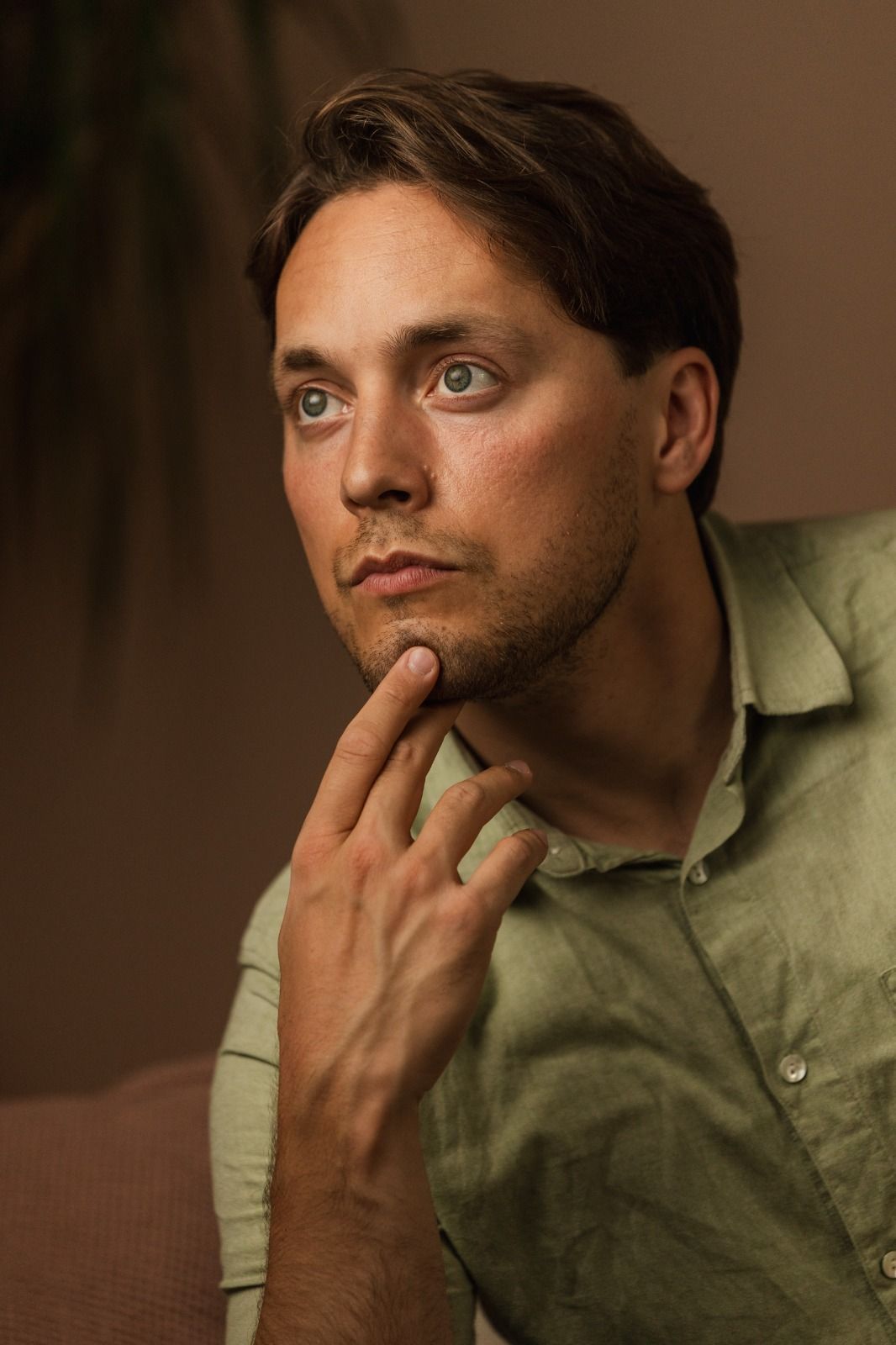 Gabriel, thoughtful, hand at his chin, in a green linen shirt.