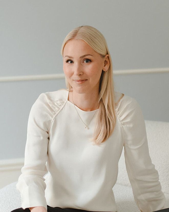 Jenny, smiling, seated on a cream sofa in a white blouse.