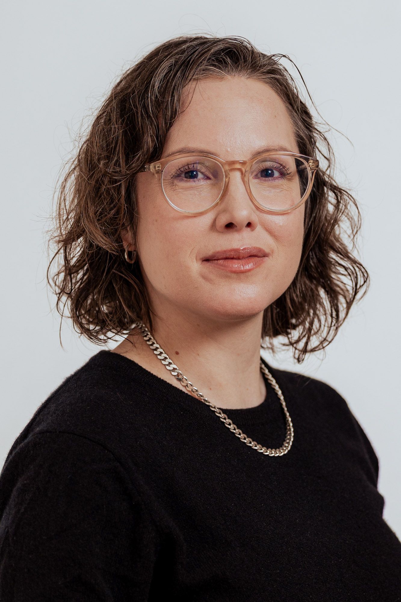 Sara, smiling, with curly hair and glasses, in a black top.